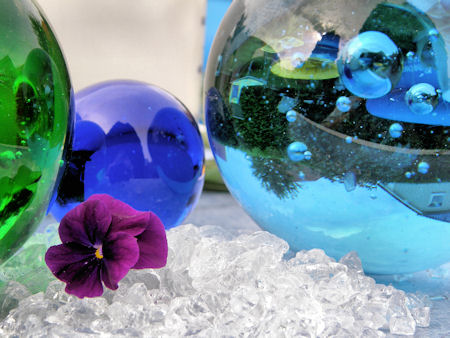 Klares Glasgranulat mit farbigen Glaskugeln und einer Blüte
