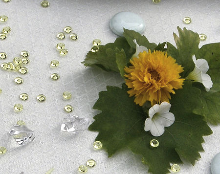 Gelbe und klare Acryldiamanten neben einem kleinen Blumengesteck
